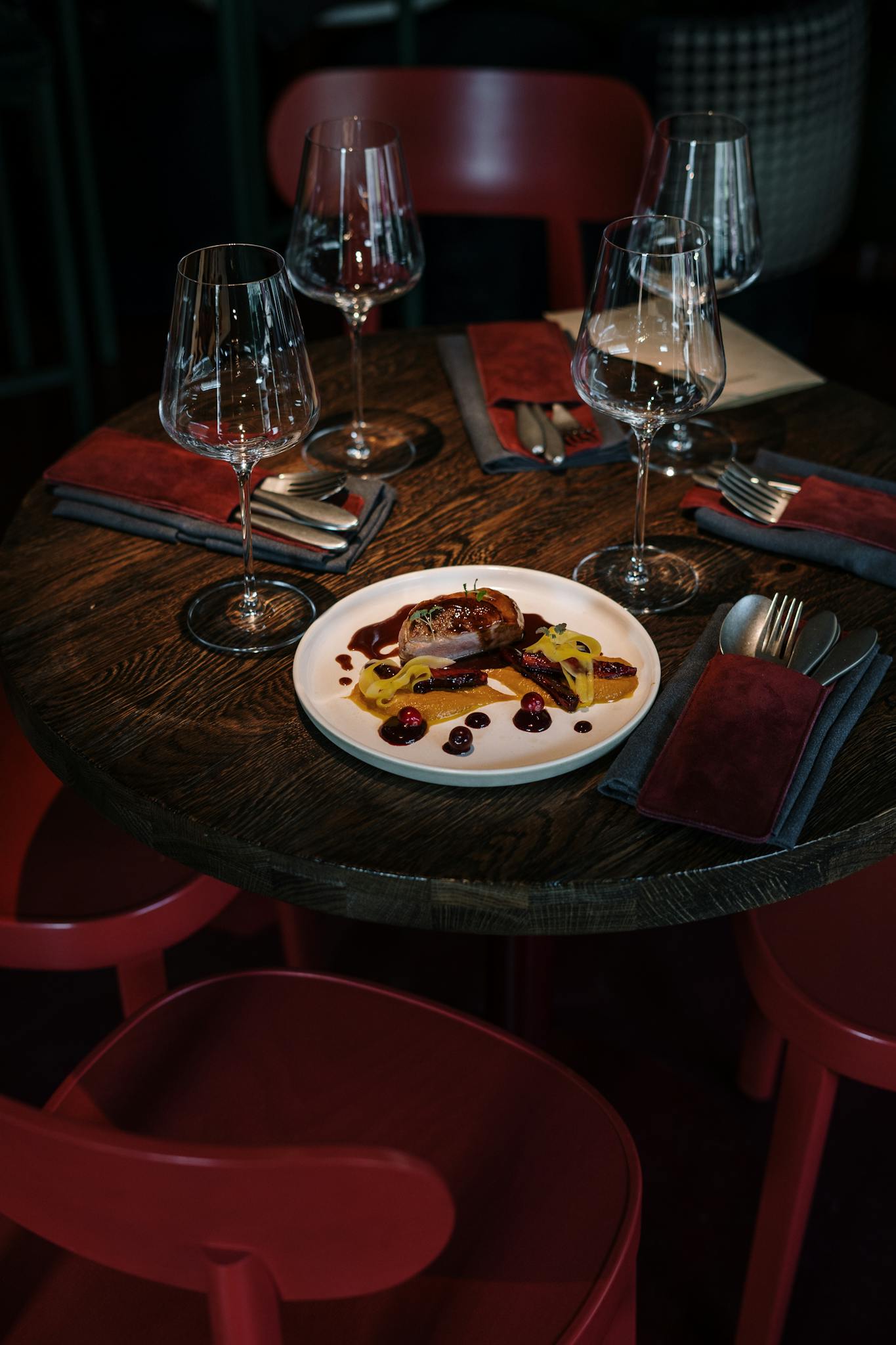 Elegant restaurant table setup featuring gourmet meat dish with wine glasses and red chairs.