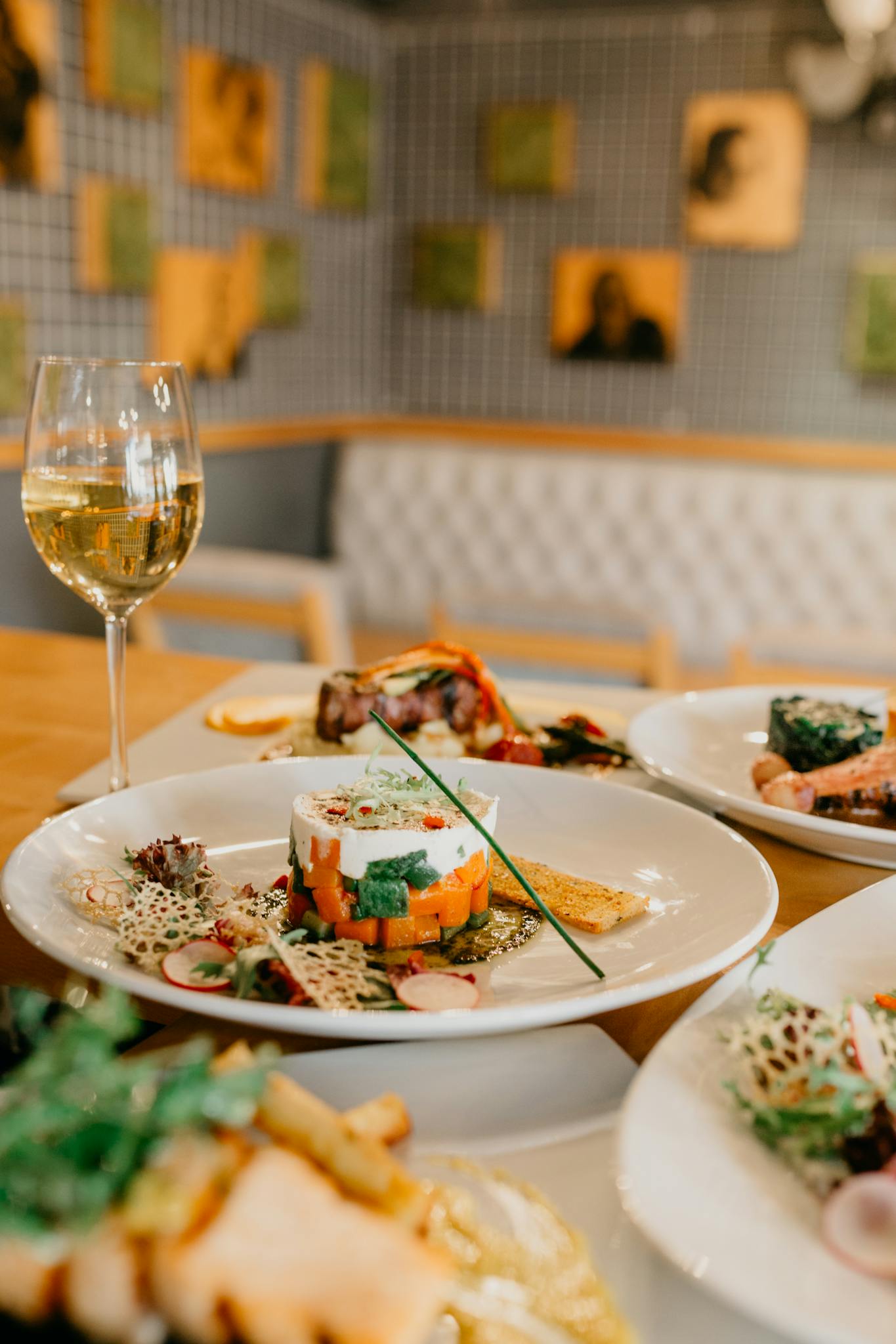Served table with various delicious dishes and glass of white wine in modern restaurant on blurred background